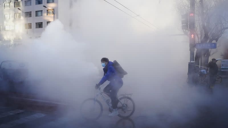 A cyclist rides through the steam leak of the water heating network in Dongcheng district during the morning rush hour in Beijing, Friday, Dec. 22, 2023. Temperatures has plunged across northern China, with a cold front moving eastward from Xinjiang in the west.