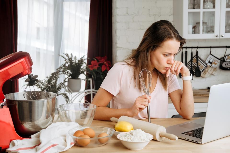 Woman cooking dessert at home and watches recipe video and tutorial on laptop.