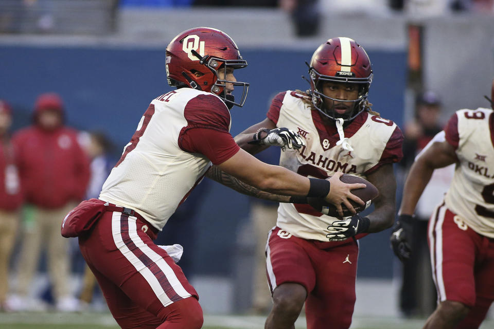 Oklahoma quarterback Dillon Gabriel (8) hands the ball off to running back Eric Gray (0) during the second half of an NCAA college football game against West Virginia in Morgantown, W.Va., Saturday, Nov. 12, 2022. (AP Photo/Kathleen Batten)