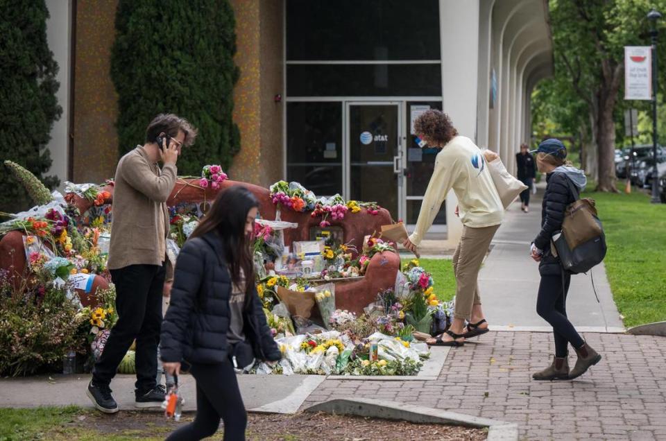 Daniel Speer, center, a UC Davis graduate student, lays a dried floral arrangement on the memorial at Compassion Bench to honor David Henry Breaux on Saturday, May 6, 2023, after visiting the Davis Farmers Market at Central Park. Breaux was found fatally stabbed April 27.