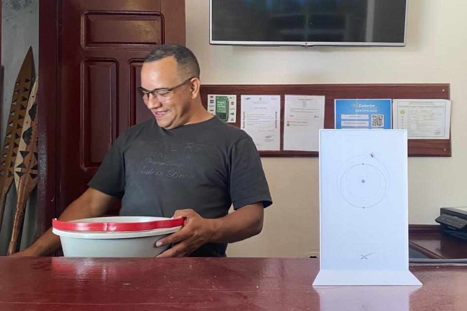 El hotelero Rubeney de Castro Alves se ve de pie junto a un router de Starlink instalado en su recepción en Atalaia do Norte, en la Amazonía brasileña, el 26 de febrero de 2023. Starlink, una división de la compañía SpaceX de Elon Musk, tiene casi 4.000 satélites en órbitas bajas que conectan a personas en rincones remotos de la Amazonía. Alves instaló el sistema en su hotel en diciembre. Ahora puede hacer transferencias bancarias y hacer videollamadas. Incluso ha empezado a ver Netflix.(AP Foto/Fabiano Maisonnave)