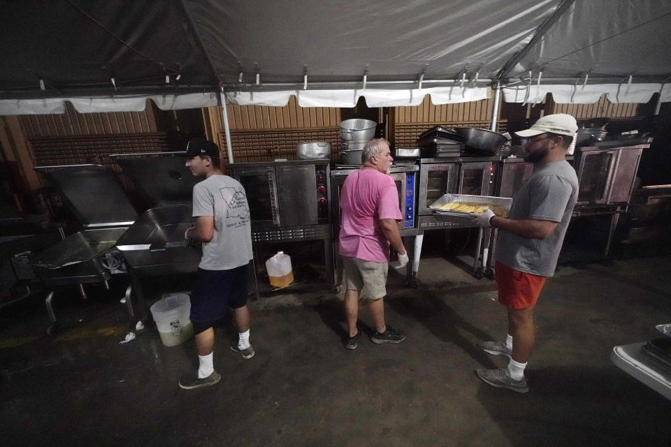 Caterer Tony Faul, center, works with Kaleb Boullion, left, and Haven Doucet as they prepare breakfast inside a tent city for electrical workers in Amelia, La., Friday, Sept. 17, 2021. In one massive white tent, hundreds of cots are spread out; experienced workers bring their own inflatable mattresses. Another tent houses a cafeteria that serves hot breakfast starting about 5 a.m., dinner and boxed lunches that can be eaten out in the field. (AP Photo/Gerald Herbert)