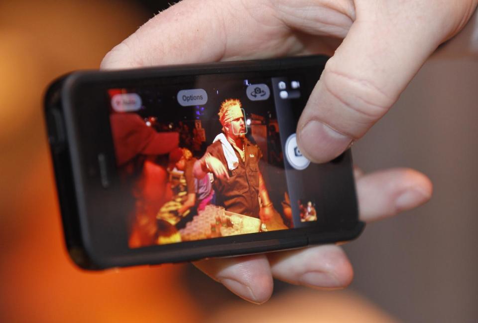 Guy Fieri is seen on a cell phone at the South Beach Wine and Food Festival's Burger Bash, Friday, Feb. 22, 2013, in Miami Beach, Fla. (AP Photo/Luis M. Alvarez)