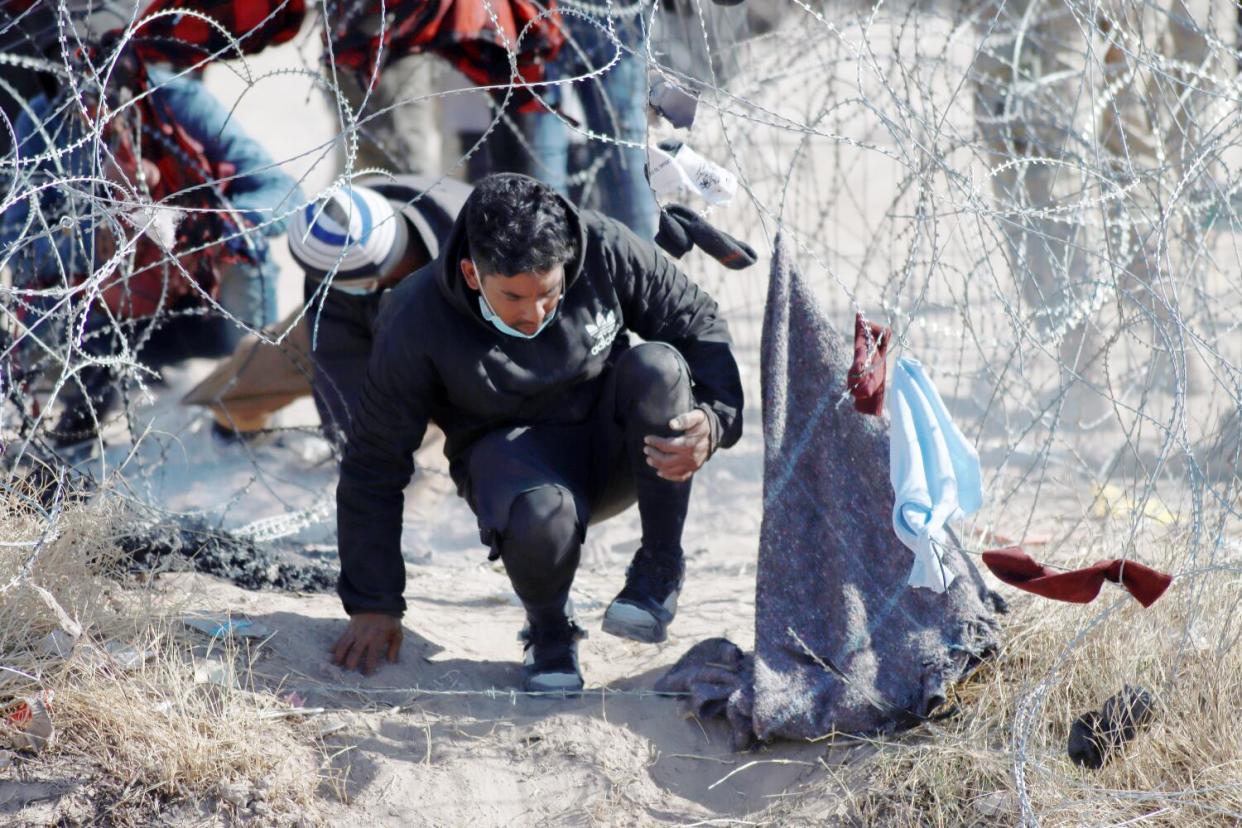 A man in a medical face mask climbs through razor wire.