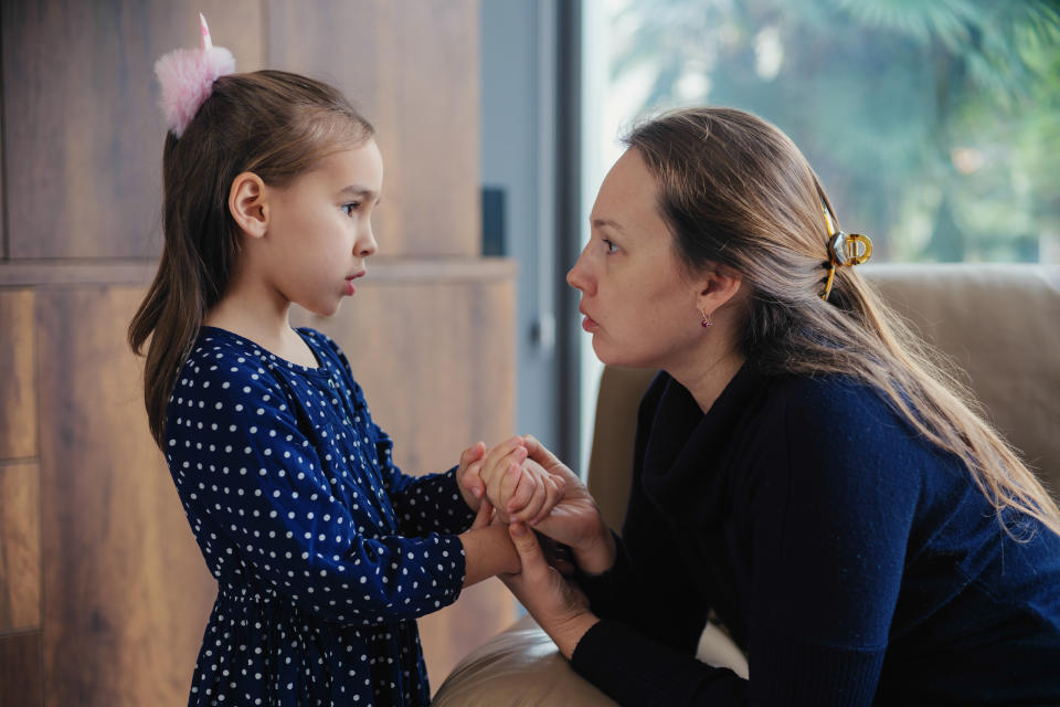 A white woman holds her young daughter's hands as she looks seriously at her, listening to what the girl has to say