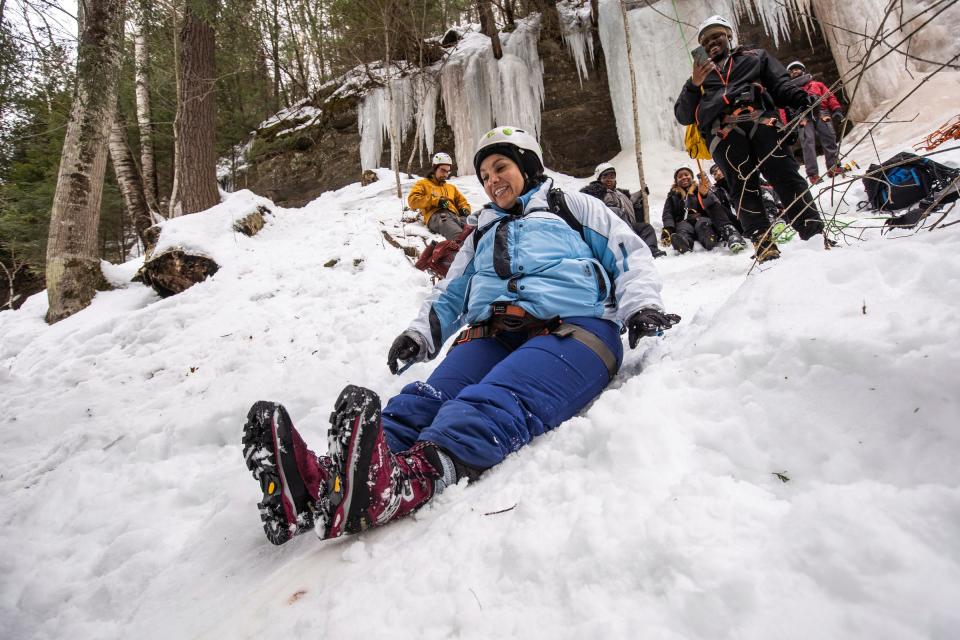 Latino Outdoors Grand Rapids member Lorena Aguayo-Marquez, left, slides down a hill to the bus after climbing The Curtains ice climbing wall in Munising during Michigan Ice Fest in Michigan's Upper Peninsula on Thursday, Feb. 9, 2023, with a group of people from Detroit Outdoors and other organizations providing the outdoor experience for people of color.