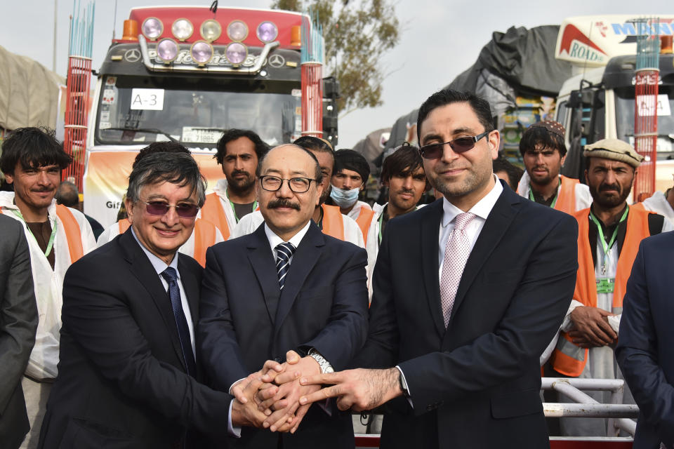 India’s foreign secretary Harsh Vardhan Shringla, center, and Afghanistan’s ambassador to India Farid Mamundzay, right, join hands as they pose before the trucks carrying wheat from India passed through the Attari-Wagah border between India and Pakistan, near Amritsar, India, Tuesday, Feb. 22, 2022. India's foreign ministry says it has sent off tons of wheat to Afghanistan to help relieve desperate food shortages, after New Delhi struck a deal with neighboring rival Pakistan to allow the shipments across the shared border. (AP Photo/Prabhjot Gill)