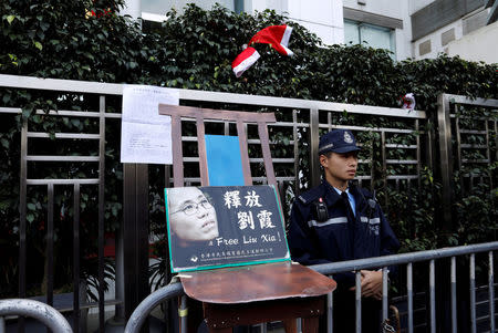 FILE PHOTO: A police officer stands guard next to a chair prop, alluding to an empty chair at late Liu Xiaobo's Nobel Peace Prize awarding ceremony in 2010, with an image of his wife Liu Xia, during a protest to urge for the release of Liu Xia, outside the Chinese liaison office in Hong Kong, China December 25, 2017. REUTERS/Tyrone Siu/File Photo