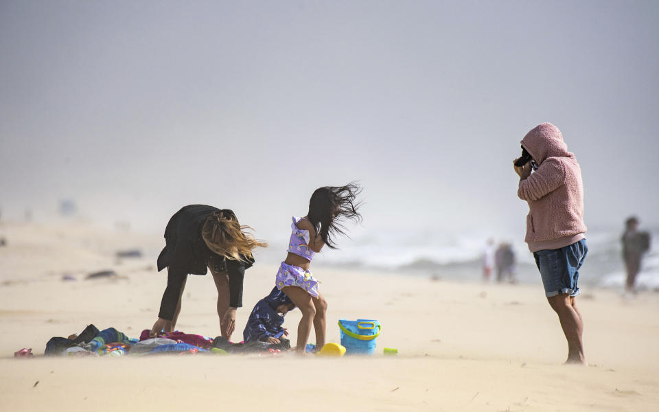 Marich Schapiro, left, her daughters, Cassie Schapiro and AJ Schapiro, and June Castillo, brave the wind as they wait for Schapiro's husband to finish surfing south of the pier in Huntington Beach, Calif., on Tuesday, Jan. 19, 2021. (Jeff Gritchen/The Orange County Register/SCNG via AP)