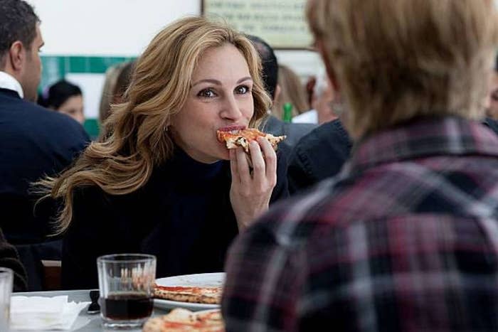 A woman eating a slice of pizza with a glass of wine.