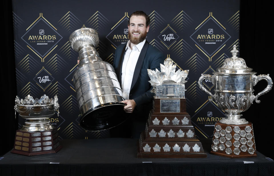 FILE - In this June 19, 2019, file photo, St. Louis Blues' Ryan O'Reilly poses with, from left, the Frank J. Selke Trophy, for top defensive forward; the Stanley Cup; the Conn Smythe Trophy, for MVP during the playoffs; and the Clarence S. Campbell Bowl, for the Western Conference playoff champions, at the NHL Awards in Las Vegas. Ryan O’Reilly stockpiled quite the hardware to show off at his Stanley Cup day. On display next to the Cup he helped the St. Louis Blues win were the Conn Smythe Trophy as playoff MVP and the Selke Trophy as the NHL’s best defensive forward. Any player would gladly celebrate with those shiny centerpieces, though O’Reilly at 28 and on his third team is only now showing he’s this kind of elite player.(AP Photo/John Locher, File)