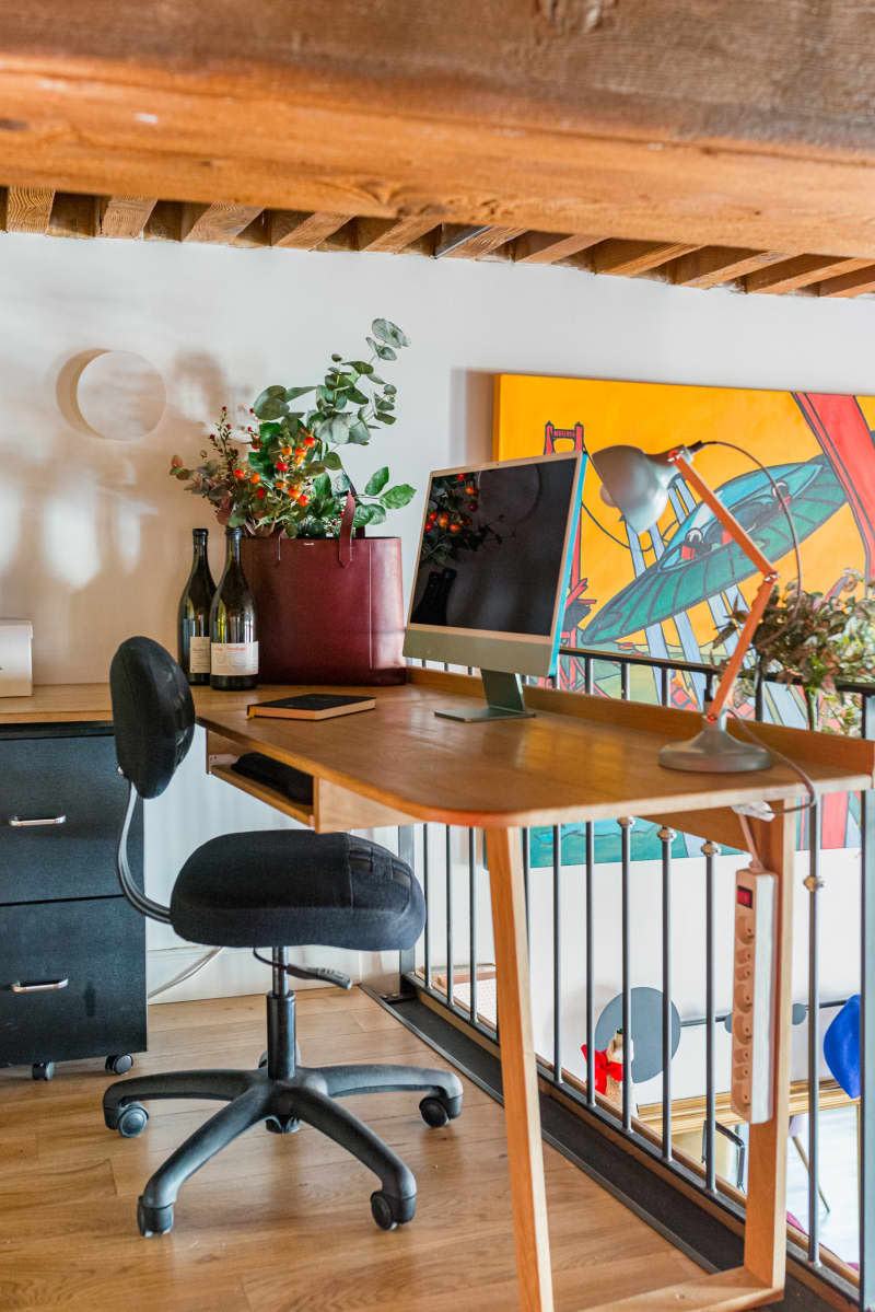 Lofted artist space with wooden desk and black office chair.