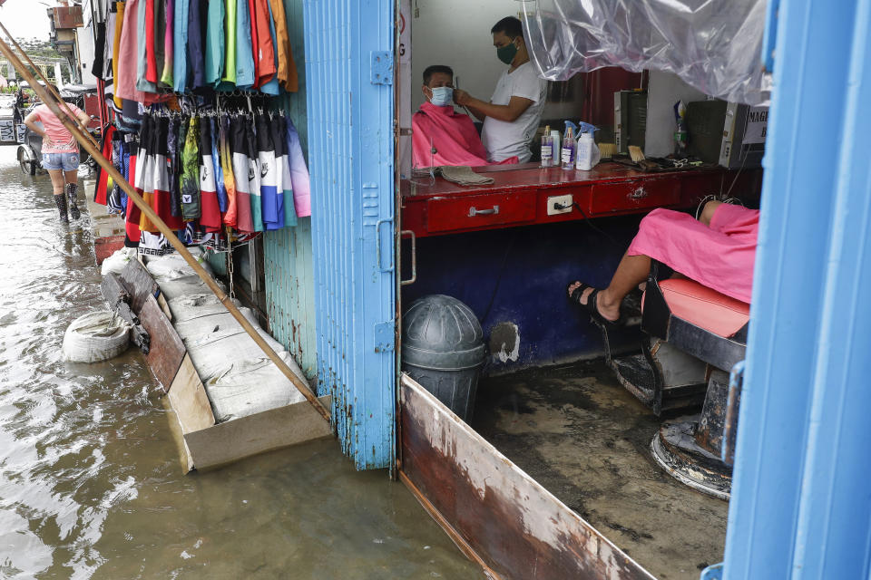 A man has his hair cut at a barbershop flooded by Typhoon Molave in Pampanga province, northern Philippines on Monday, Oct. 26, 2020. The fast moving typhoon has forced thousands of villagers to flee to safety in provinces. (AP Photo/Aaron Favila)