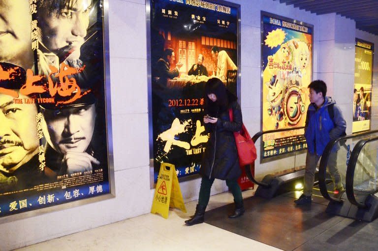 A woman (L) walks past film advertisements at a cinema in Beijing on January 18, 2013. Ten new movie screens open each day in China as the popularity of cinema soars in the country, but the appeal of Chinese films has failed to maintain the pace