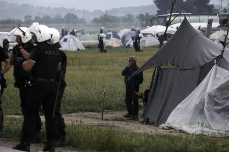 A refugee smokes as riot policemen stand amidst tents during a police operation at a refugee camp at the border between Greece and Macedonia, near the village of Idomeni, Greece, 24 May 2016. REUTERS/Yannis Kolesidis/Pool