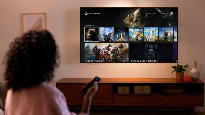 A woman holding a remote while looking at an Amazon Fire TV with the Xbox app on it. It's on the Cloud Gaming menu with Fallout 76, Senua's Saga: Hellblade 2, and more on it.