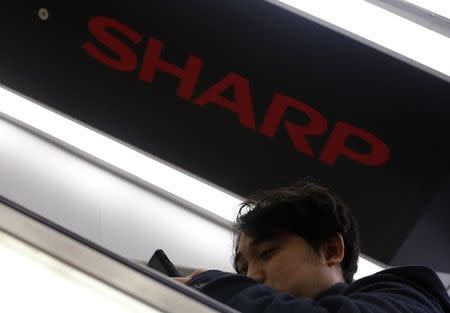 A shopper using a smartphone rides an escalator past under a logo of Sharp Corp at an electronics shop in Tokyo March 3, 2015. REUTERS/Yuya Shino