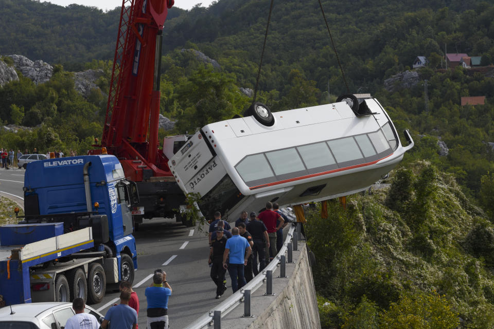 Rescue workers remove a bus at the accident site on a road near Cetinje, Montenegro, Tuesday, Sept. 19, 2023. A British national and another person were killed Tuesday and nine people were seriously injured in Montenegro when a bus plunged into a ravine, authorities said. The bus was carrying some 30 passengers when it swerved on a steep road around noon, police said. (AP Photo/Risto Bozovic)