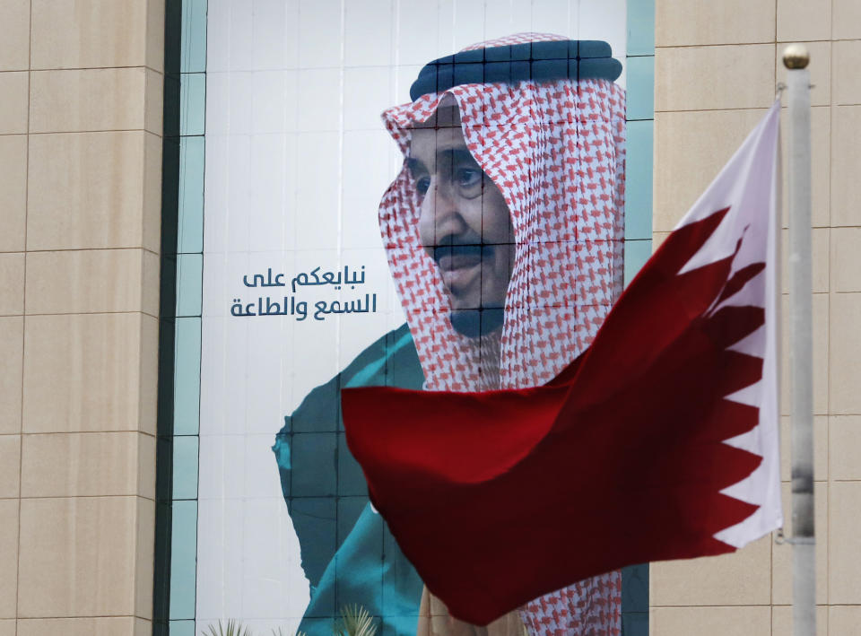 FILE - In this Dec. 9, 2019, file photo, a Qatari flag flies in front of a banner showing Saudi King Salman with Arabic writing that reads, "We pledge you to listen and obey" at a trade center in Riyadh, Saudi Arabia, ahead of the Gulf Cooperation Council "GCC", 40th summit. Kuwait's foreign ministry on Monday, Jan. 4, 2021, announced that Saudi Arabia will lift a years-long embargo on Qatar, opening its air and land borders in the first steps toward ending the Gulf crisis.(AP Photo/Amr Nabil, File)