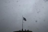 A Greek national flag flutters atop the Athens Acropolis hill as tourists take photos during a snowstorm February 10, 2015. REUTERS/ Alkis Konstantinidis
