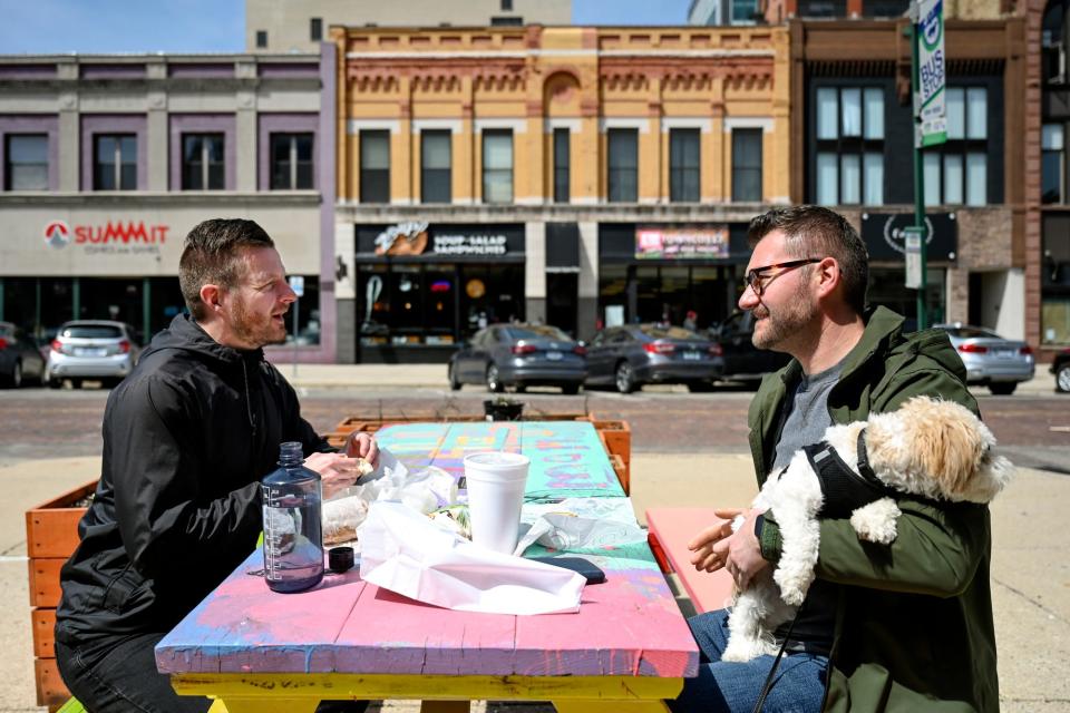 Christopher Roe, left, and Jonathan Shotwell, along with dog Leo, eat lunch outside on South Washington Square on Friday, April 29, 2022, in downtown Lansing.