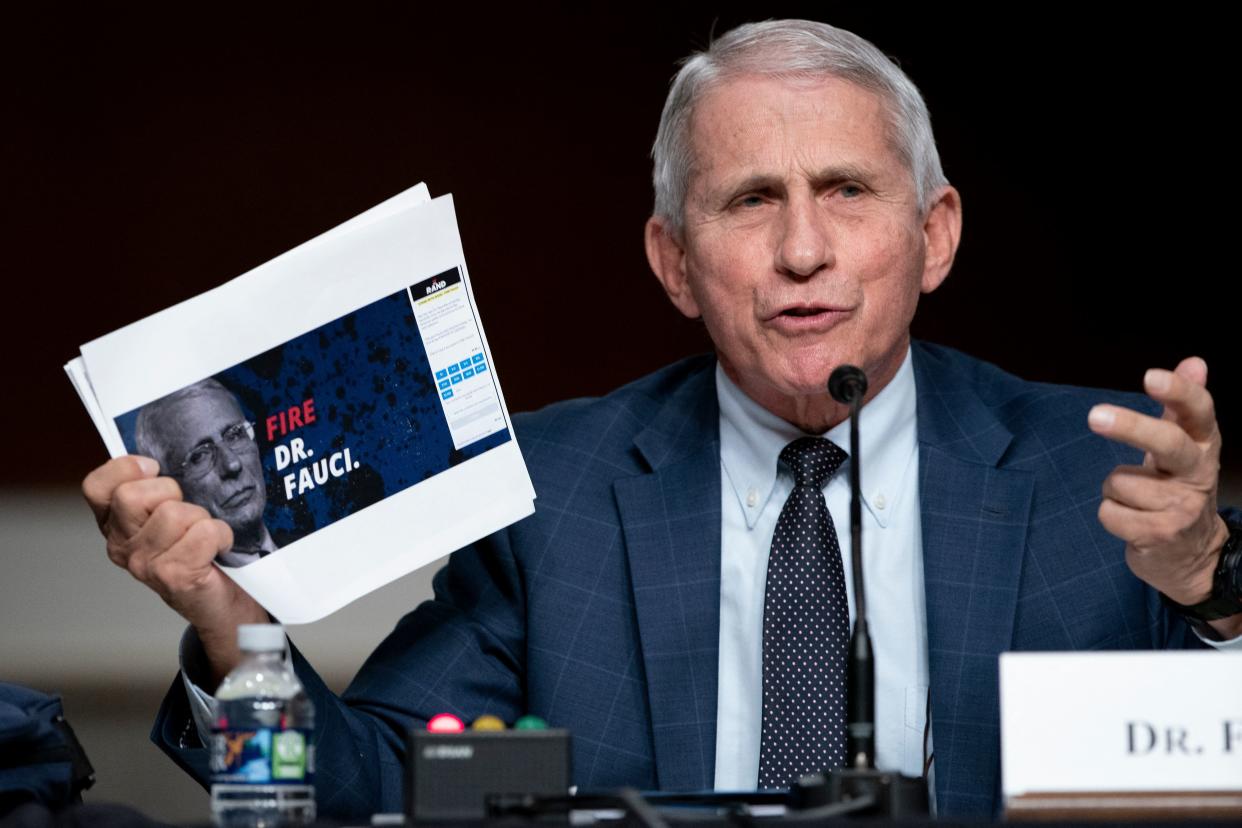 Dr. Anthony Fauci holds a printout with the words: Fire Dr. Fauci.