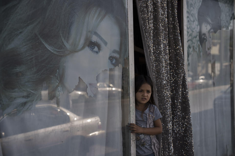 An Afghan girl looks out from a beauty salon in Kabul, Afghanistan, Thursday, Sept. 16, 2021. Since the Taliban gained control of Kabul, several images depicting women outside beauty salons have been removed or covered up. (AP Photo/Felipe Dana)