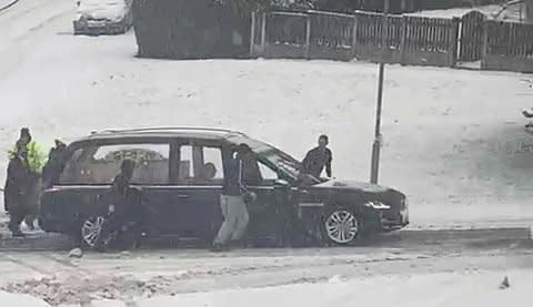 A group of strangers help a hearse up a hill after it got stuck in the snow. (Michelle Mulcahy/SWNS)