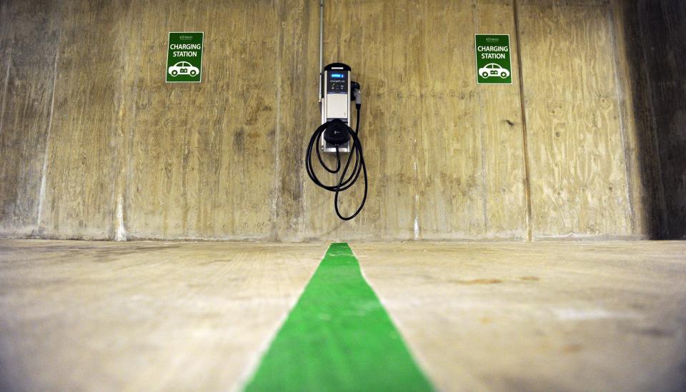 A charging station is mounted on a wall, with a long cable ready to insert in an electric vehicle.