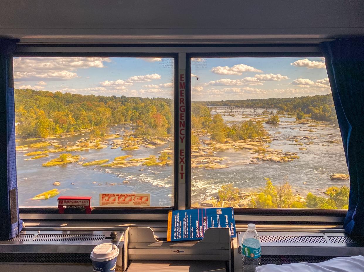 A view out the window of an Amtrak train shows trees, marshes, and clouds in a blue sky