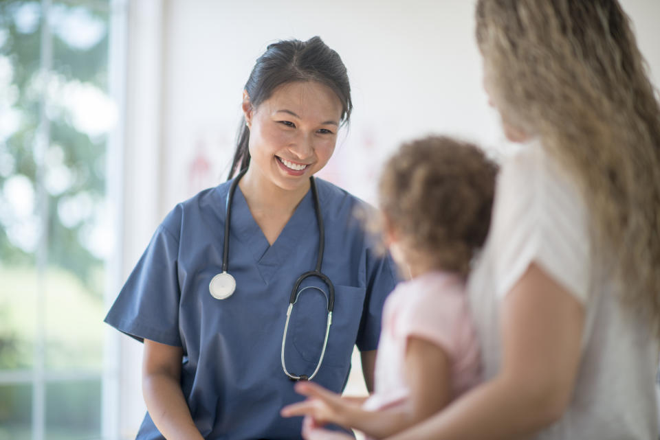 A smiling physician smiling at a child being held by their parent