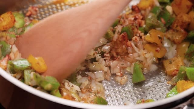 Frying seasoned onion, capsicum, and garlic in a frying pan with wooden spatula