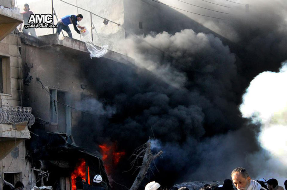 In this citizen journalism image provided by Aleppo Media Center (AMC), an anti-Bashar Assad activist group, and authenticated based on its contents and other AP reporting, a Syrian man, top left, tried to extinguish a fire with a bucket of water at shops following a Syrian government forces warplane attack, at al-Bab neighborhood in Aleppo, Syria, Saturday, Feb. 1, 2014. Syrian military helicopters dropped barrels packed with explosives on rebel-held areas of the northern city of Aleppo on Saturday, killing at least a dozen of people including a family trapped in a car, as government forces inched closer to opposition-held areas. (AP Photo/Aleppo Media Center, AMC)