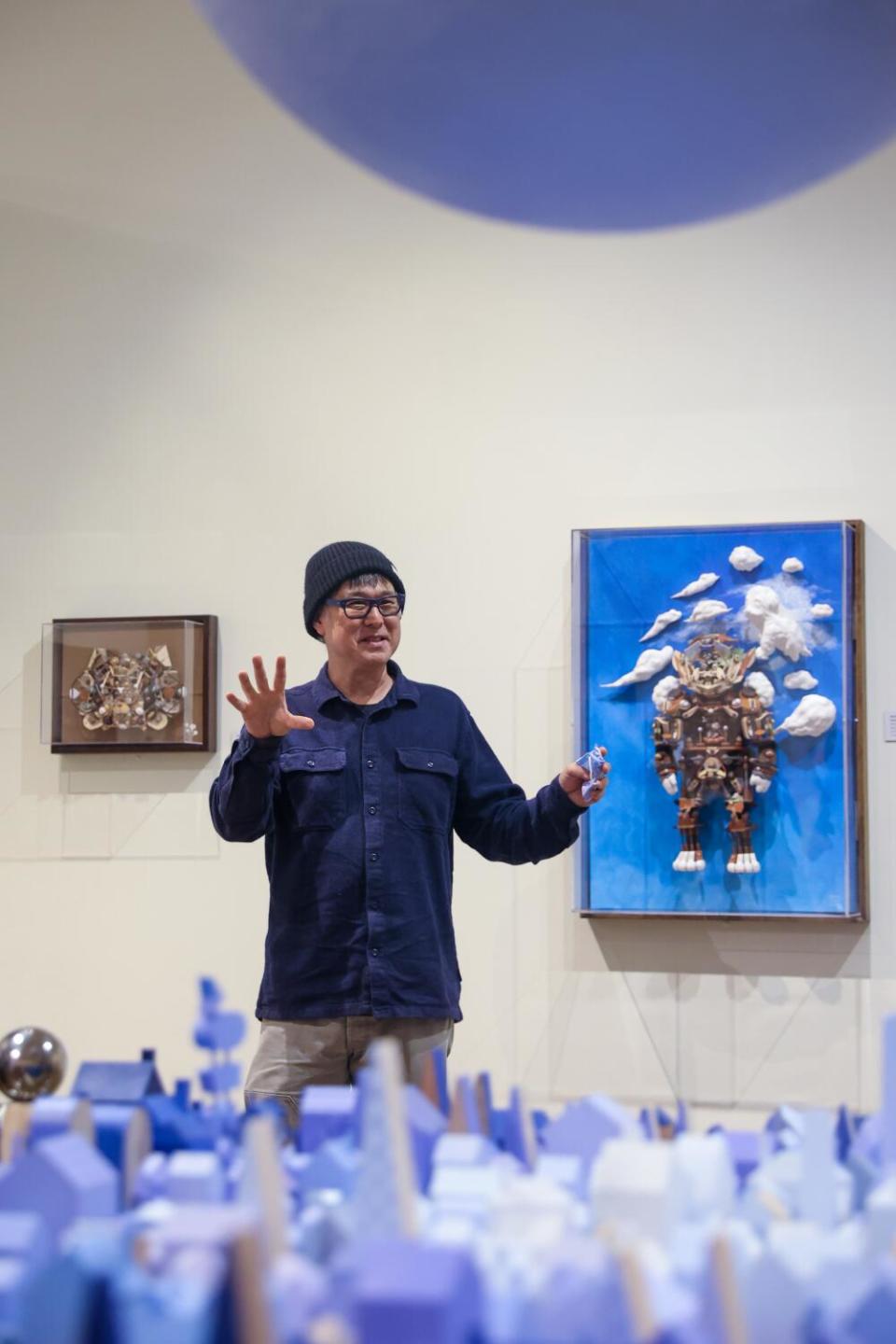 A man gestures in front of a painting at a museum.