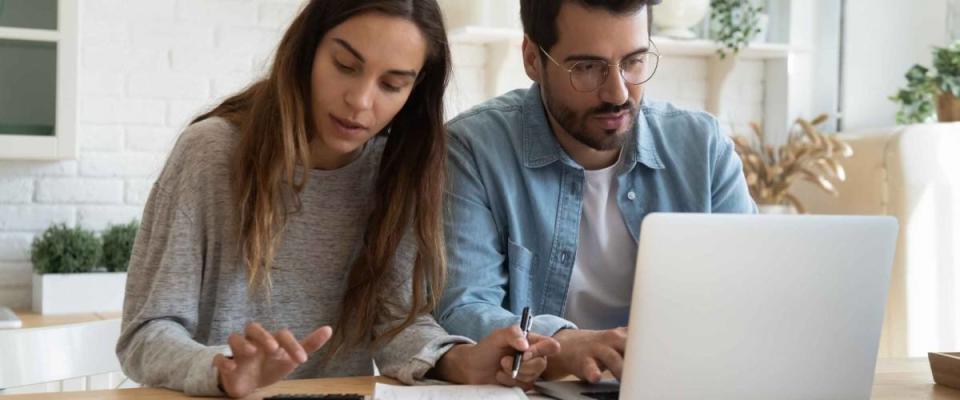 Serious man and woman calculating bills, using calculator and laptop, online banking services, family discussing and planning budget, focused wife and husband checking finances together