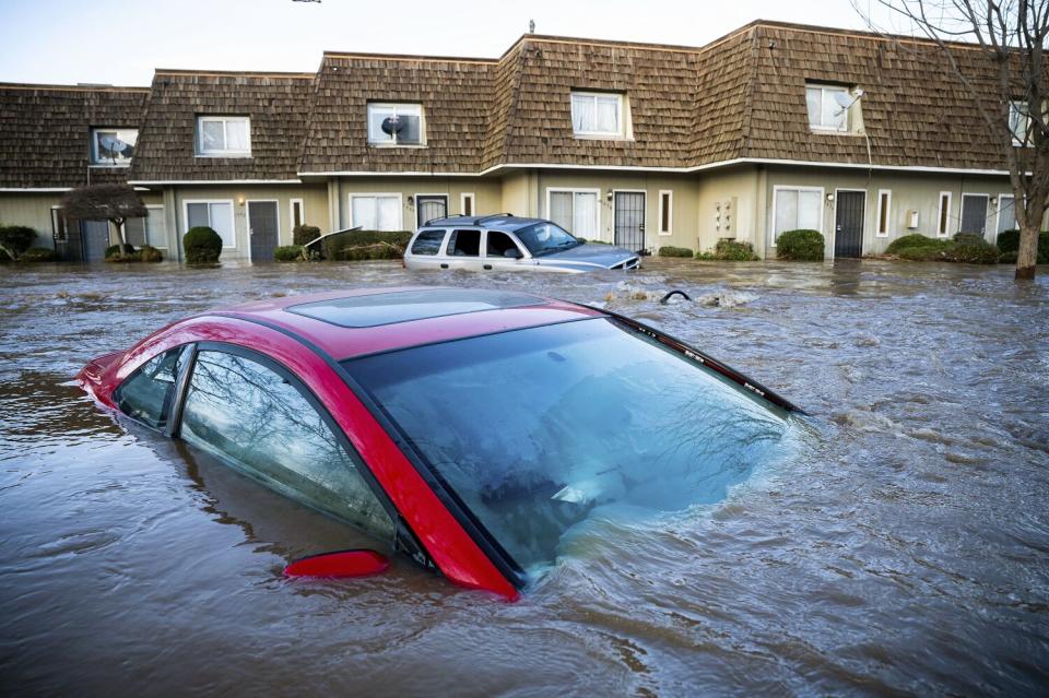 Floodwaters course through a neighborhood in Merced on Tuesday, submerging cars.