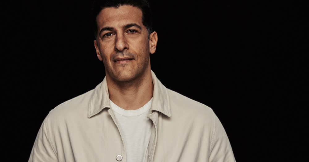 Actor Simon Kass, looking at the camera wearing a shirt, on a black background.