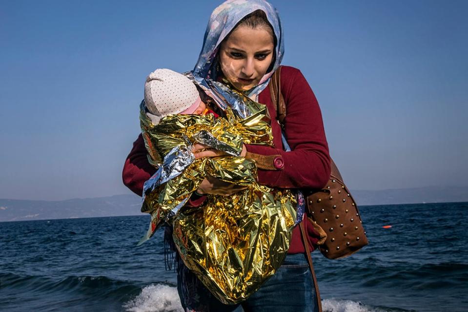 A young Syrian mother holds her child wrapped in a thermal blanket after disembarking on the shore of Lesbos, Greece, November 2015.