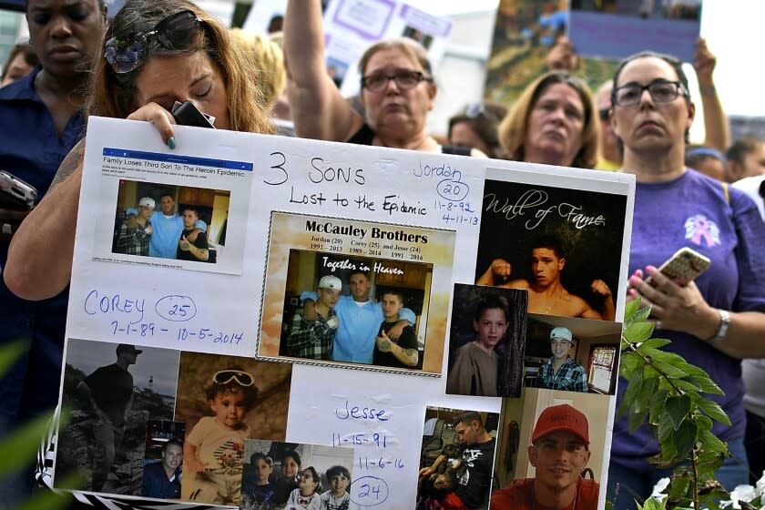 Jeanmarie McCauley, left, of Rockland, Mass., rests her head on a sign she made of her three children who died within three years to drug addiction, as family and friends who lost loved ones to OxyContin and opioid overdoses stage a protest outside the headquarters of Purdue Pharma in Stamford, Conn., on Friday, Aug. 17, 2018. (AP Photo/Jessica Hill)