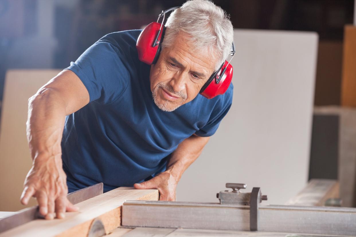 concentrated senior male carpenter cutting wood in workshop