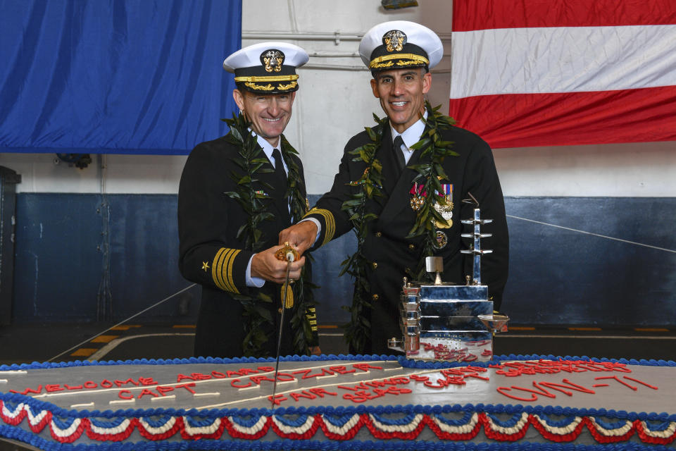 In this Nov. 19, 2019, photo provided by the U.S. Navy, Capt. Brett Crozier, left, then the new commanding officer of the aircraft carrier USS Theodore Roosevelt (CVN 71), and outgoing Capt. Carlos Sardiello cut a cake in the ship's hangar bay during a change of command ceremony reception. Crozier relieved Sardiello to become the 16th commanding officer of Theodore Roosevelt. Sardiello was called on to step in as commander of the Roosevelt after Crozier was fired for sending an email pleading with commander to act more quickly to address the growing outbreak on the ship. (Seaman Apprentice Olympia O. McCoy/U.S Navy via AP)