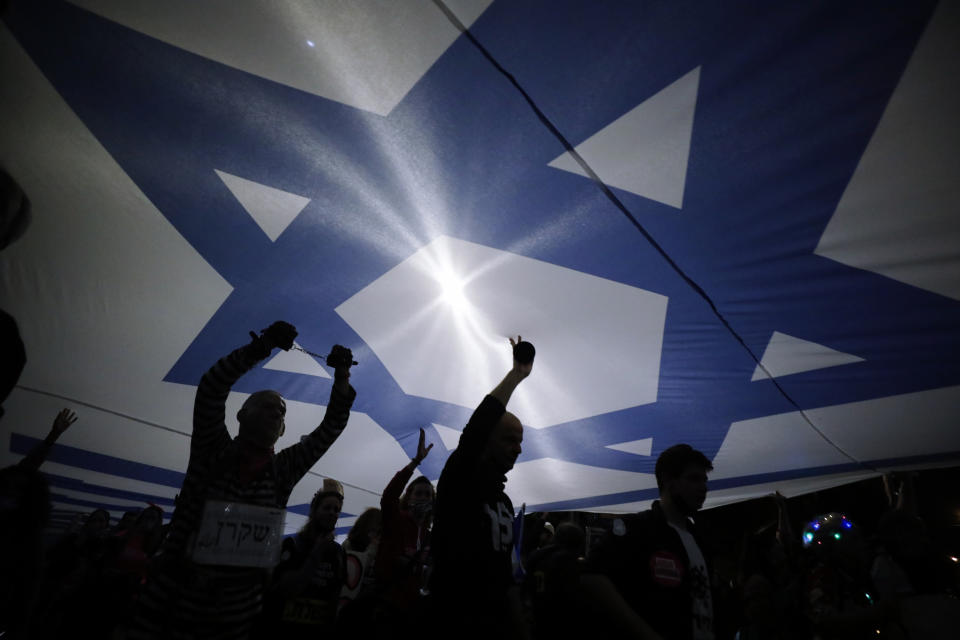 Israeli protesters carry large Israeli flag during a demonstration against Israeli Prime Minister Benjamin Netanyahu In Jerusalem, Saturday, March. 20, 2021. The weekly protests against Netanyahu's corruption charges and his handling of the pandemic have persisted since summer, but tonight's gathering is the last before Israel will be holding its fourth election in two years on March 23. (AP Photo/Sebastian Scheiner)