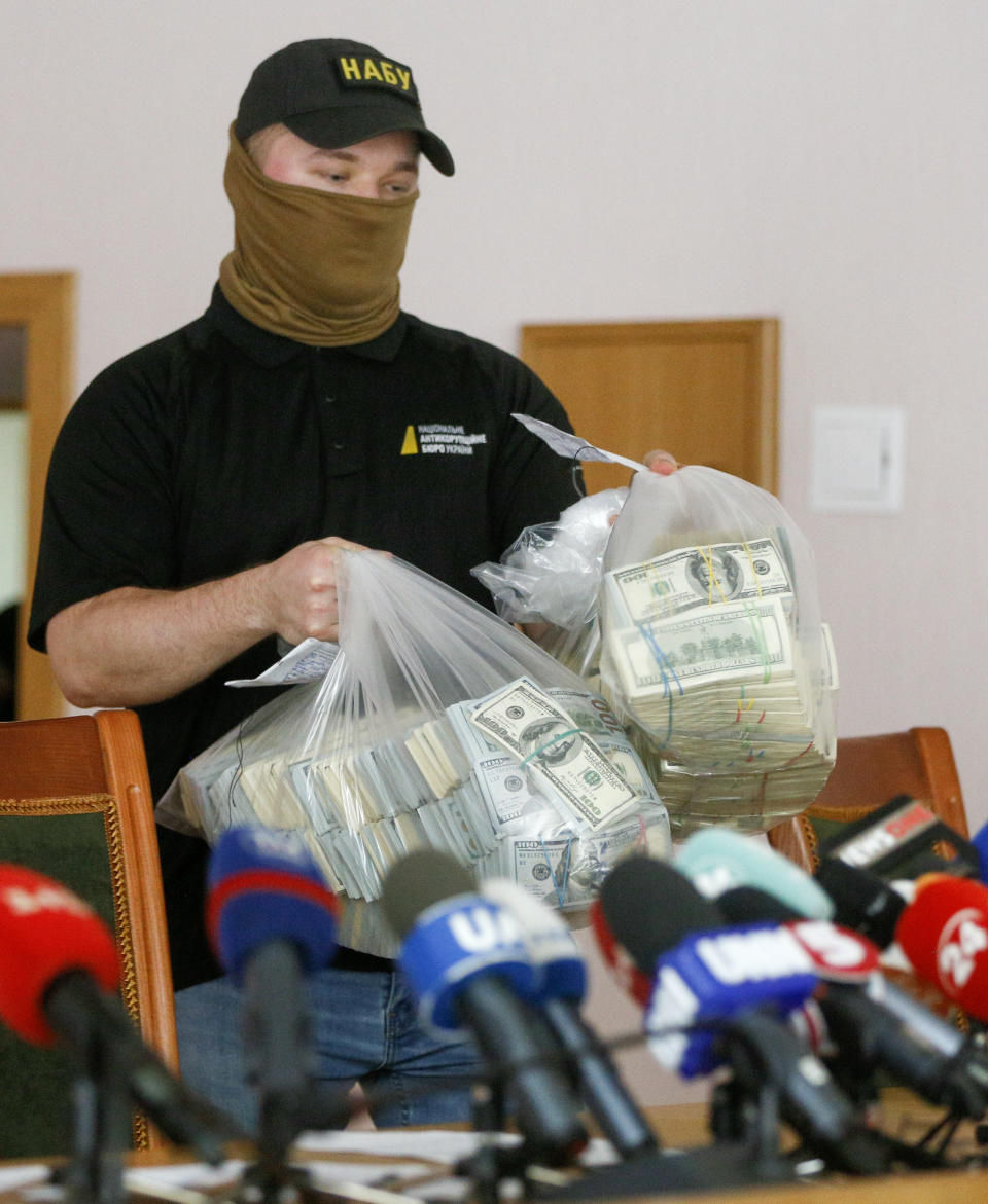A police officer holds USD 6 million in plastic bags at a briefing in an anti-corruption prosecutor's office in Kyiv, Ukraine, Saturday, June 13, 2020. Ukrainian authorities say they have intercepted a $6 million bribe attempt at dropping a criminal investigation against the head of the Burisma natural gas company where former US Vice President Joe Biden's son once held a board seat. (AP Photo/Efrem Lukatsky)