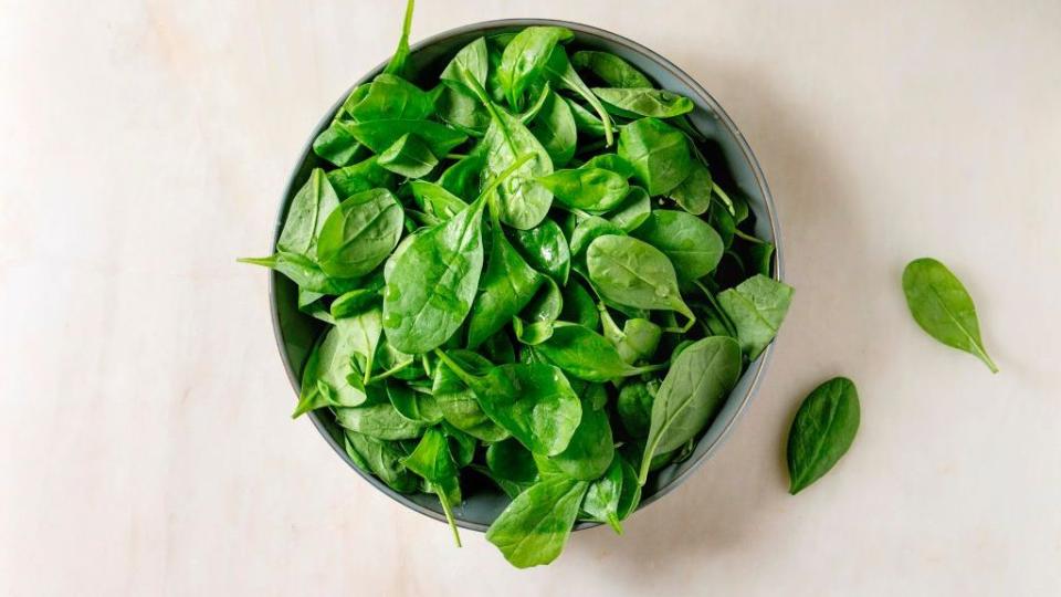bowl of fresh baby spinach leaves over white marble background flat lay copy space