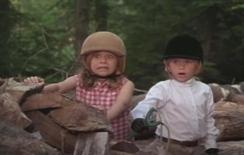 Alyssa and Amanda wear riding clothes and look horrified while standing behind stacks of chooped wood