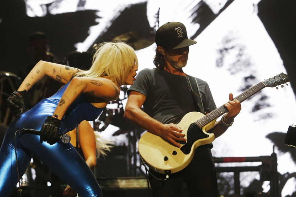 Miley leaning over toward her guitarist onstage