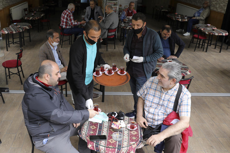 Waiters wearing face masks to protect against coronavirus, serves clients at a theahouse, in Ankara, Turkey, Monday, June 1, 2020. Restaurants and cafes welcomed sit-in customers, beaches and museums reopened as Turkey's broadest easing of coronavirus restrictions came into effect.(AP Photo/Burhan Ozbilici)