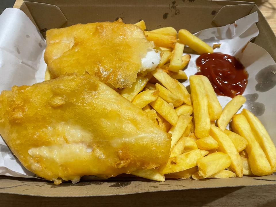 A cardboard box filled with battered, fried fish, french fries, and a dollop of ketchup. The fish looks golden brown.