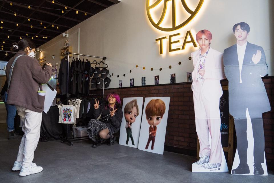 People pose for a photo squatting next to K-pop decor. Two standees depict K-pop artists.