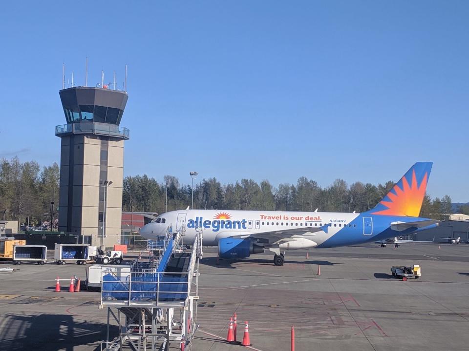 An Allegiant plane at an airport next to the control tower.